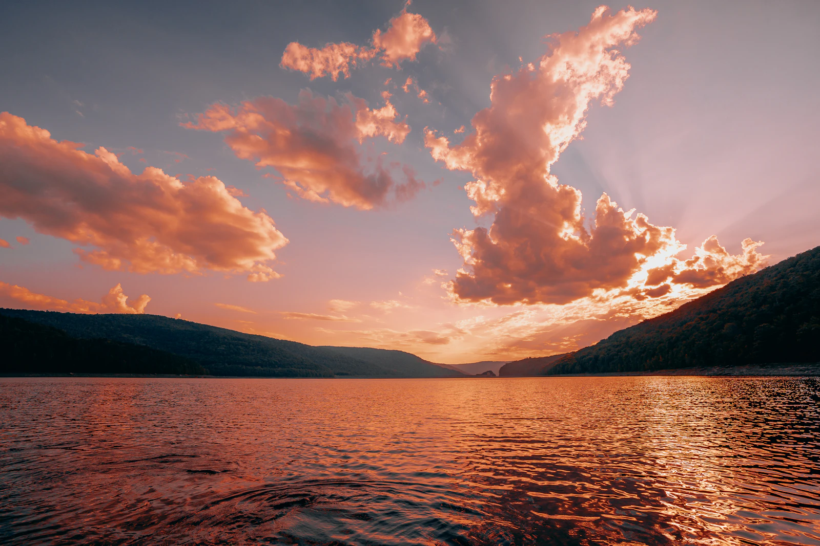 Lago refletindo o pôr do sol entre montanhas; fotografia ilustrativa, sem associação a uma localidade da notícia.